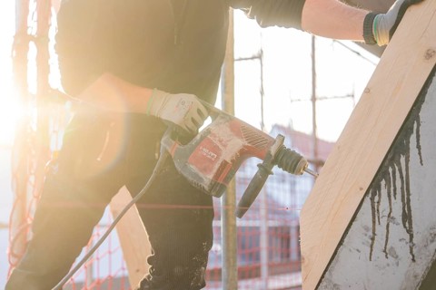 Construction worker drilling wood elements on construction site in sunlight, carpentry construction