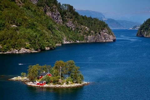 Small island with house in Lovrafjord, surrounded by blue water and green hills