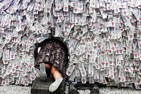 Person crawling through hole in stone with strips of paper in Yasui Konpiragu Temple, Kyoto, Gion,