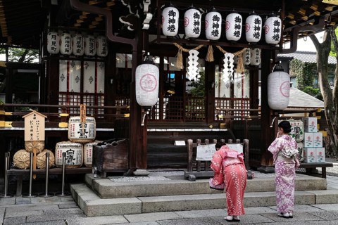 Two woman wearing kimono praying to traditional lanterns at Yasui Konpiragu Temple, Kyoto, Gion,