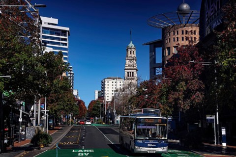 Queen Street with bus traffic, skyscrapers and clock tower under clear sky, Auckland, New Zealand