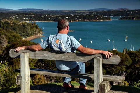 A man is sitting relaxed on a bench and enjoying the view of the Bay of Islands, Maiki, Bay of