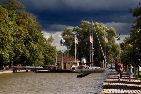 Söderköping harbour on Göta Canal with flags and trees under a cloudy sky, Söderköping, Sweden