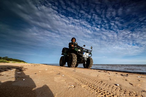 Person riding on ATV along the beach under a cloudy sky, Kolka, Latvia