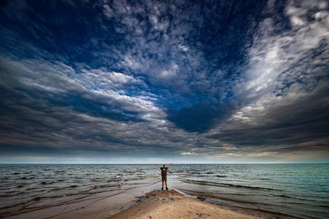 Man on sandy beach with dramatic clouds above sea near Cape Kolka, Kolka, Latvia