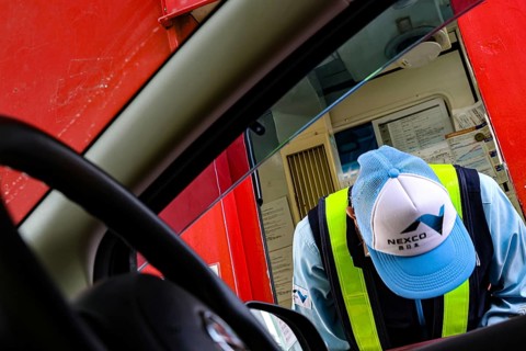 Worker wearing cap and vest bends kindly in front of a car, Kobe, Hyogo, Japan