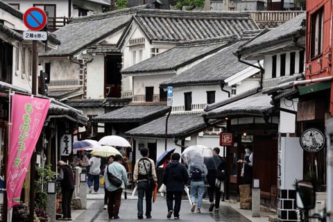 People with umbrellas walk through a historic street with traditional buildings in Kurashiki,