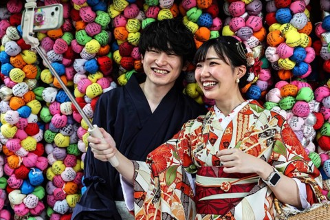 Couple wearing kimonos taking selfies in front of colorful backgrounds at Yasaka Koshindo Temple,