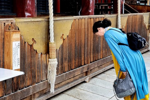Woman praying in front of a massive wooden shrine at Yasaka-jinja Temple, Kyoto, Higashiyama, Japan