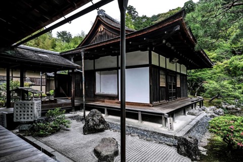 Zen garden with traditional pavilion surrounded by carefully arranged rocks and green vegetation,