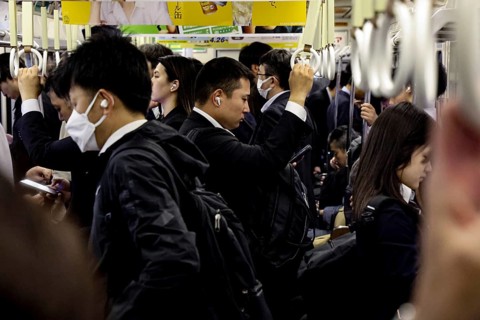 Commuters crowd the Osaka subway, many wearing suits and using smartphones, Osaka, Japan