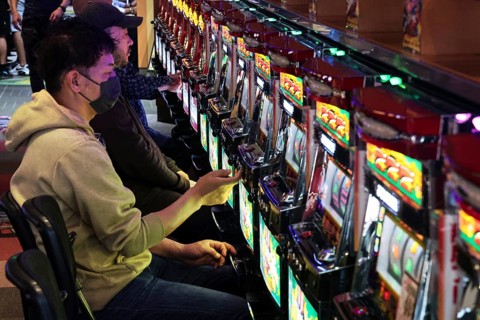 Men playing pachinko on sparkling machines, intense game atmosphere, Osaka, Japan