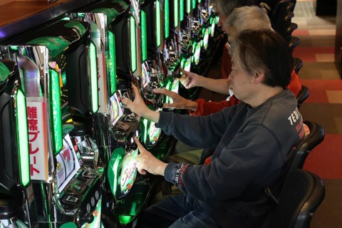 Men play pachinko on bright machines in a lively setting, Osaka, Japan