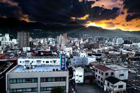Dramatic city view of Beppu at sunset with mountains and dense buildings, Beppu, Japan