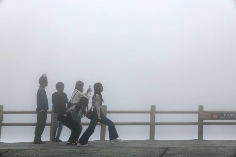 Tourists pose in front of fog-covered crater in Aso, Aso, Japan