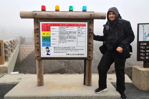 Person standing next to a warning sign in the fog of Nakadake Crater, Aso, Kumamoto, Japan