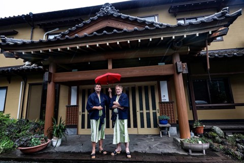 Two people with red umbrellas in front of a traditional ryokan in Aso, Aso, Kumamoto, Japan