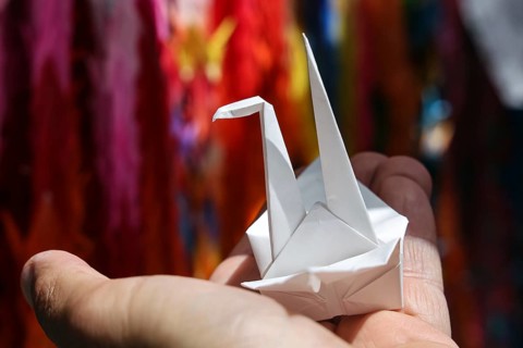 An origami crane is held by one hand in Hiroshima Peace Park, Hiroshima, Japan