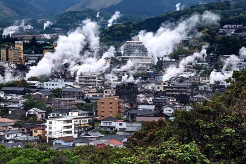 Urban landscape crossed by columns of steam, mountains in the background, Beppu, Oita, Japan