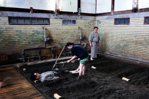 A sand bath at Takegawara Onsen Beppu, one person being cared for by another, Beppu, Oita, Japan