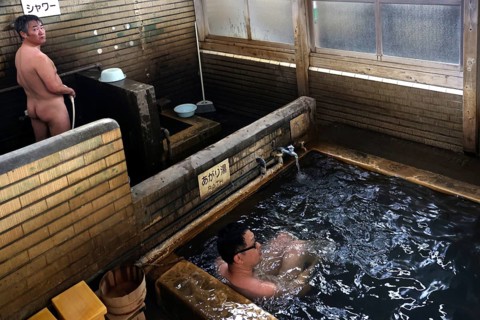 Traditional Japanese onsen bath with wooden walls in a warm setting. People enjoy the relaxing