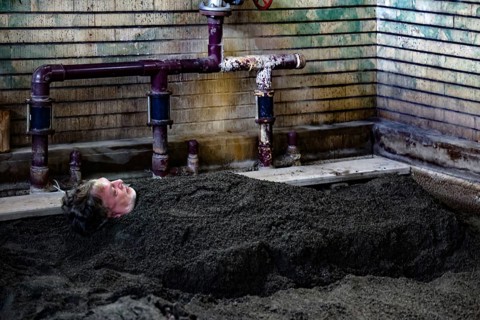 Person buried in sand in traditionally designed onsen area, Beppu, Takegawara Onsen, Japan