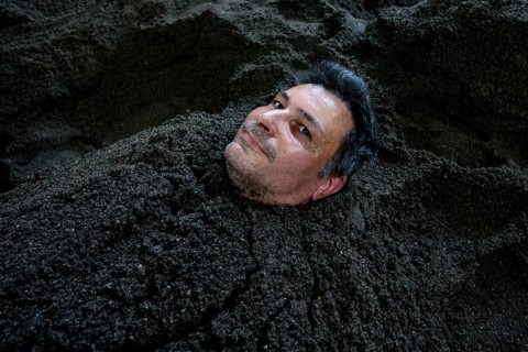 Man buried in sand bath with only his head sticking out, relaxed expression, Beppu, Takegawara