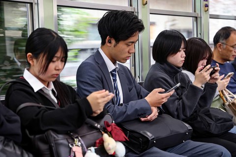 Passengers on a train in Kyoto, including a salaryman, use their smartphones, Arashiyama, Kyoto,