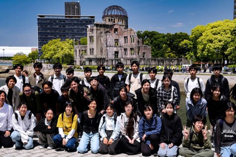 Group of students posing in front of the Hiroshima Memorial in bright sunshine, Hiroshima, Japan