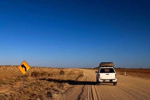 White car on a dusty road with curve sign in the vast outback, Oodnadatta, null, Australia