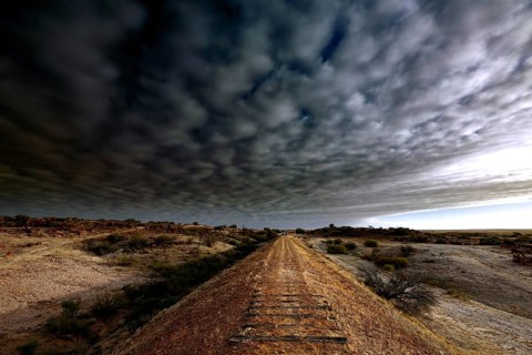Railway track under dramatic cloud cover in the evening light of the Australian outback, Oodnadatta