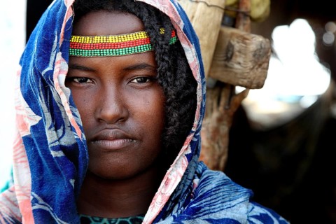 Aishe poses in traditional clothes and colorful accessories in front of Muhammad's hut in Ahmedela,