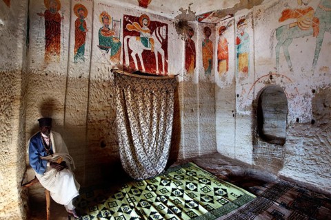 Priest sits in the richly decorated rock church Abba Daniel Krokor, zero