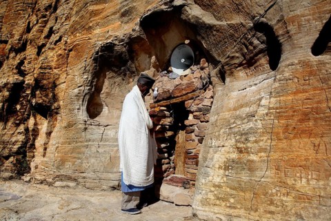 Priest stands in front of the rock church Abba Daniel Krokor in traditional clothing, zero