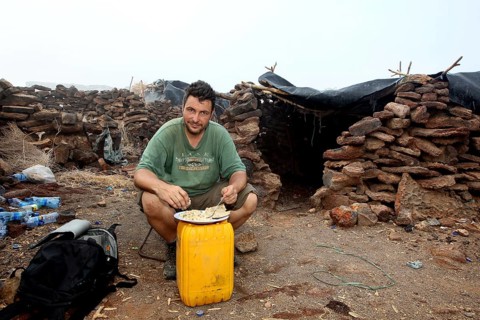 Man sitting in a warehouse of stone huts with minimalistic furniture, zero