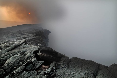 Smoke rises from a crater in a volcanic landscape, zero