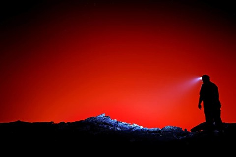 Silhouette of a human with head light against a bright red background, Erta Ale, Ethiopia