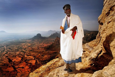 Abba Tesfay in traditional clothing with a view of the expanse of the Gheralta Mountains, Gheralta