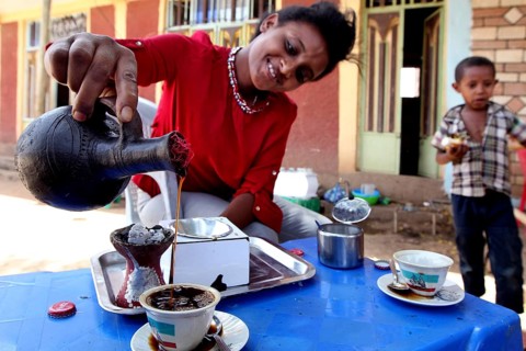 Woman preparing coffee ceremony in Mayzebri, Ethiopia while a child watches, Mayzebri, Ethiopia