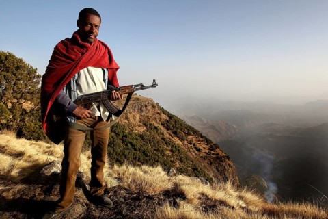 Armed companion stands in front of a vast mountain panorama in Semien Mountain National Park,