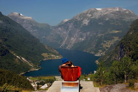 Tourist sits on a red chair and looks at the impressive panorama of Geirangerfjord, Flydalsjuvet,