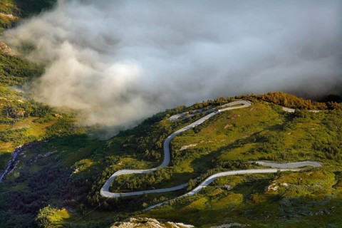 Serpentine road snakes through fog-covered green hills, Geirangerfjord, Dalsnibba, Norway