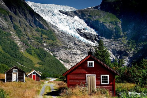 Red and white huts in front of the majestic Bøyabreen Glacier Range, surrounded by green mountains,