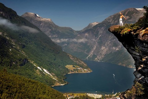 Adventurous tourist stands on cliff and enjoys views of Geirangerfjord, Flydalsjuvet,
