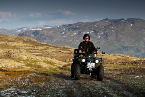 Person driving an ATV through a rugged mountain landscape under cloudy sky, zero