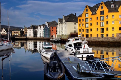 Colourful buildings and boats are reflected in the calm waters of Ålesund Harbour, Ålesund, Møre og