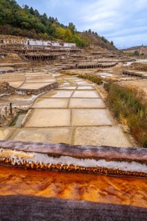 Traditional salt evaporation ponds creating white salt crystals and saline water, showcasing the