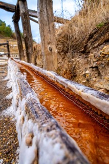 Close up view of the reddish brine flowing along a wooden channel encrusted with salt deposits at