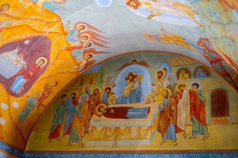 Vivid frescoes in a church depict biblical scenes with angels and saints in bright colors, domed