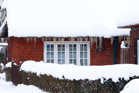 Icicles on an old thatched house covered with snow during snow flurries in winter,